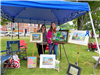 two woman standing with a group of paintings and quilts